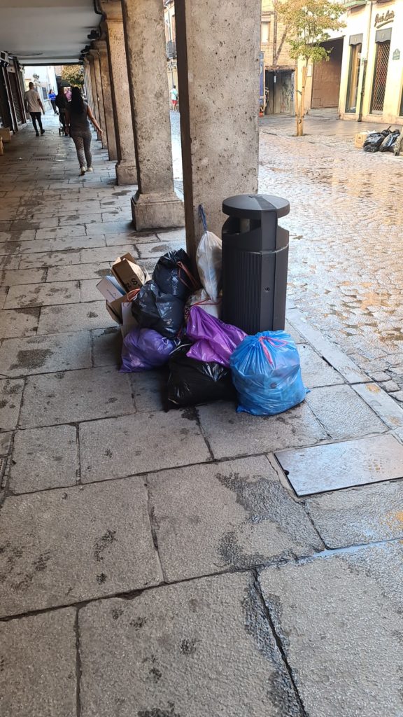 Bolsas de basura junto a una columna en la calle Mayor